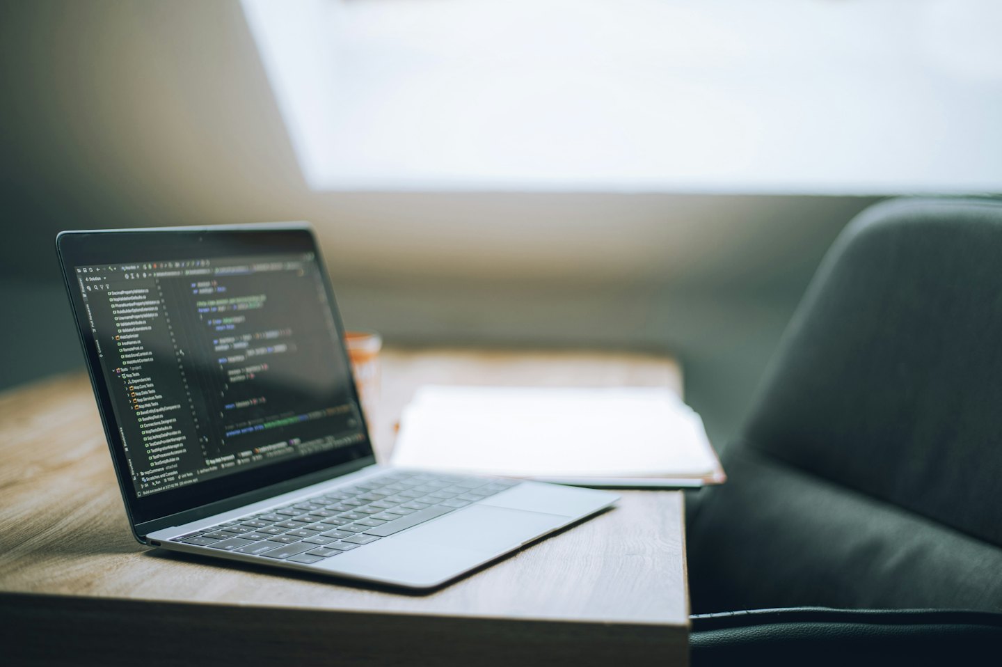 Laptop met programmeercode op een houten bureau.
